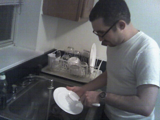 A real photograph of a modern man washing a plate in a home kitchen